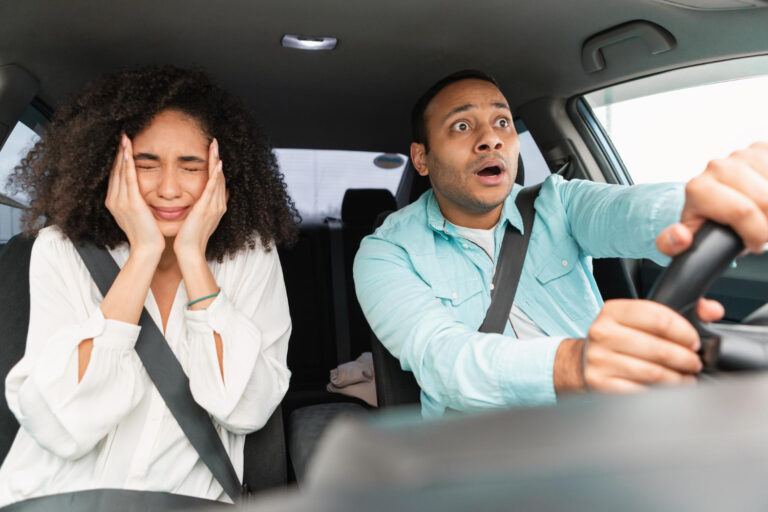 Pareja asustada en coche: hombre conduce con sorpresa, mujer se tapa los oídos