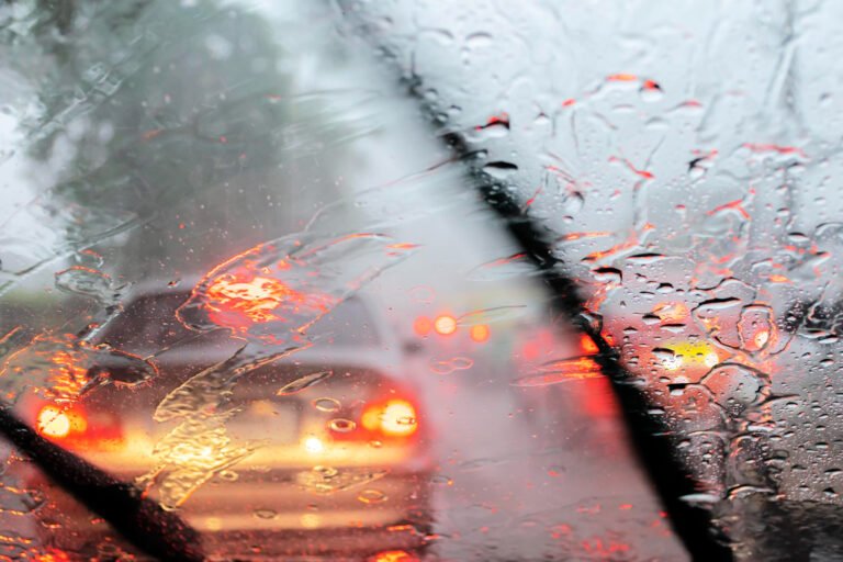 Vista a través del parabrisas mojado de autos con luces rojas de freno en tráfico bajo la lluvia.