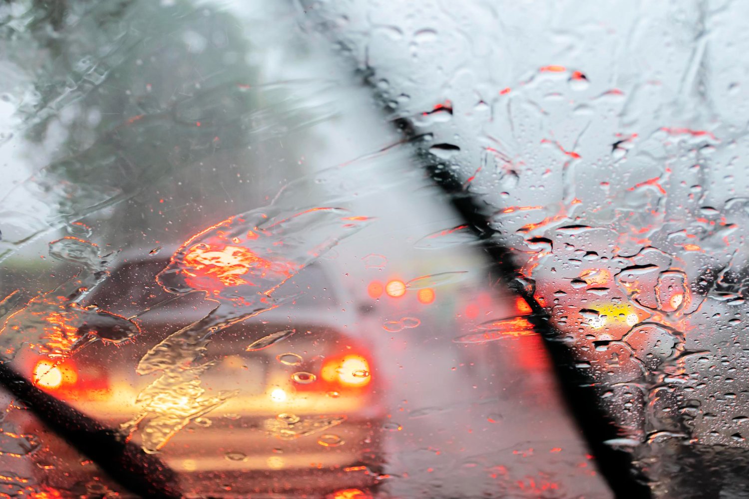 Vista a través del parabrisas mojado de autos con luces rojas de freno en tráfico bajo la lluvia.