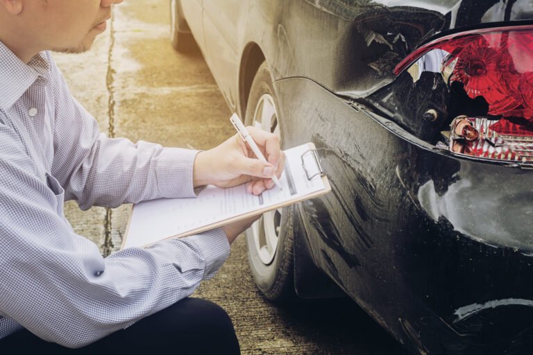 Ajustador de seguros documentando daños en un coche negro accidentado