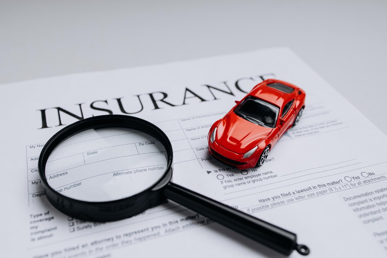 Seguro de auto: lupa sobre formulario de reclamo e auto rojo