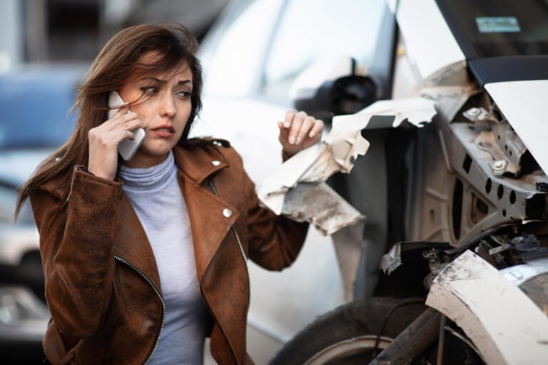 Mujer preocupada habla por teléfono junto a coche accidentado